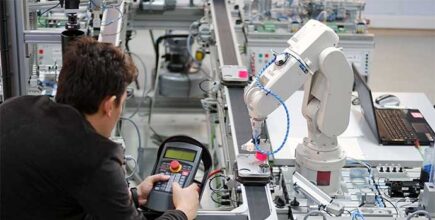 Schneider & Company - A technician programs a robotic arm in an industrial setting, showcasing the intersection of human skill and automation technology.